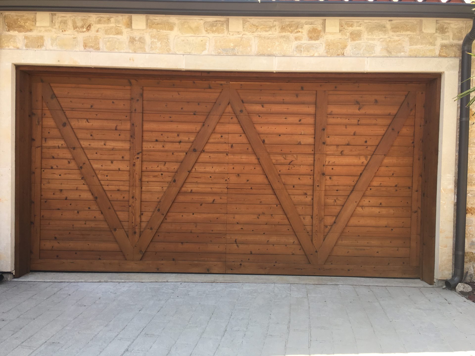 cedar-door-upright Cedar carriage-style garage door with diagonal panels on a stone home