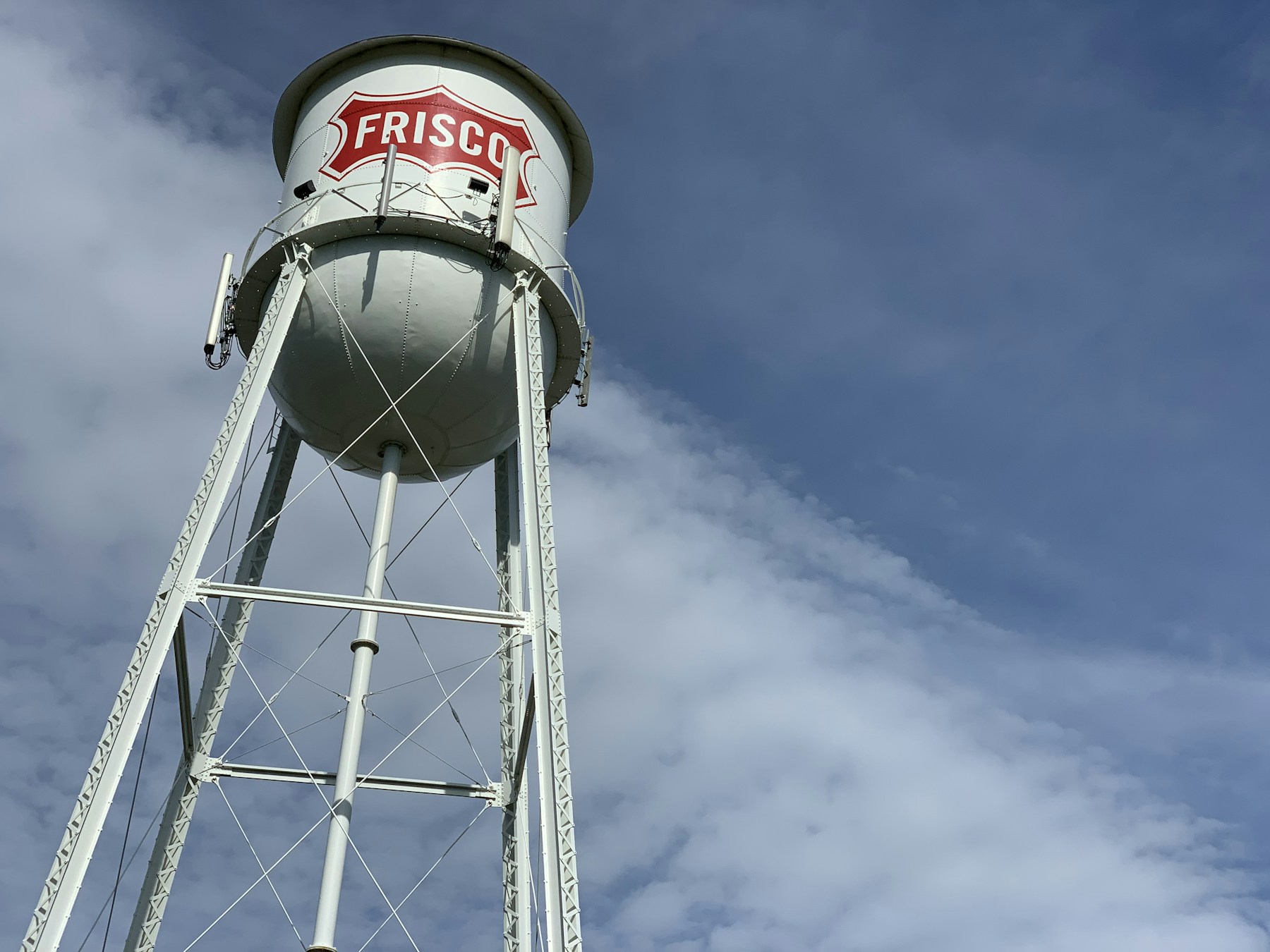 White Frisco water tower with a red sign against a cloudy sky