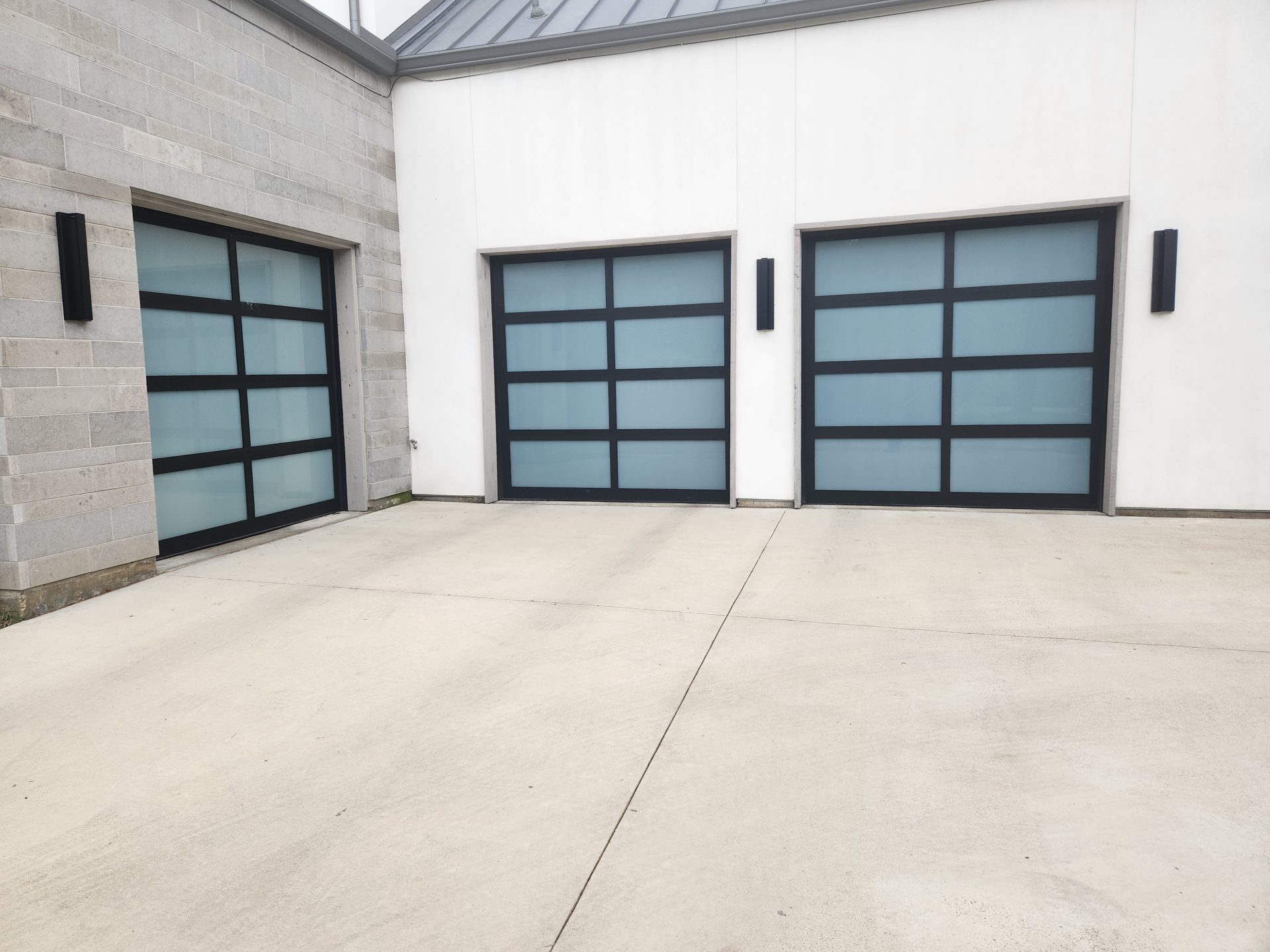 Black aluminum-framed garage doors with frosted glass panels on a contemporary home